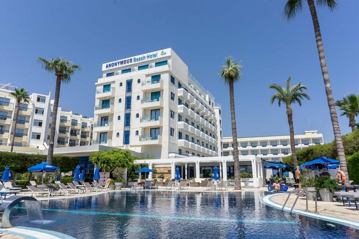 Außenbereich des Anonymous Beach Hotels mit Swimmingpool, Sonnenliegen und Palmen.