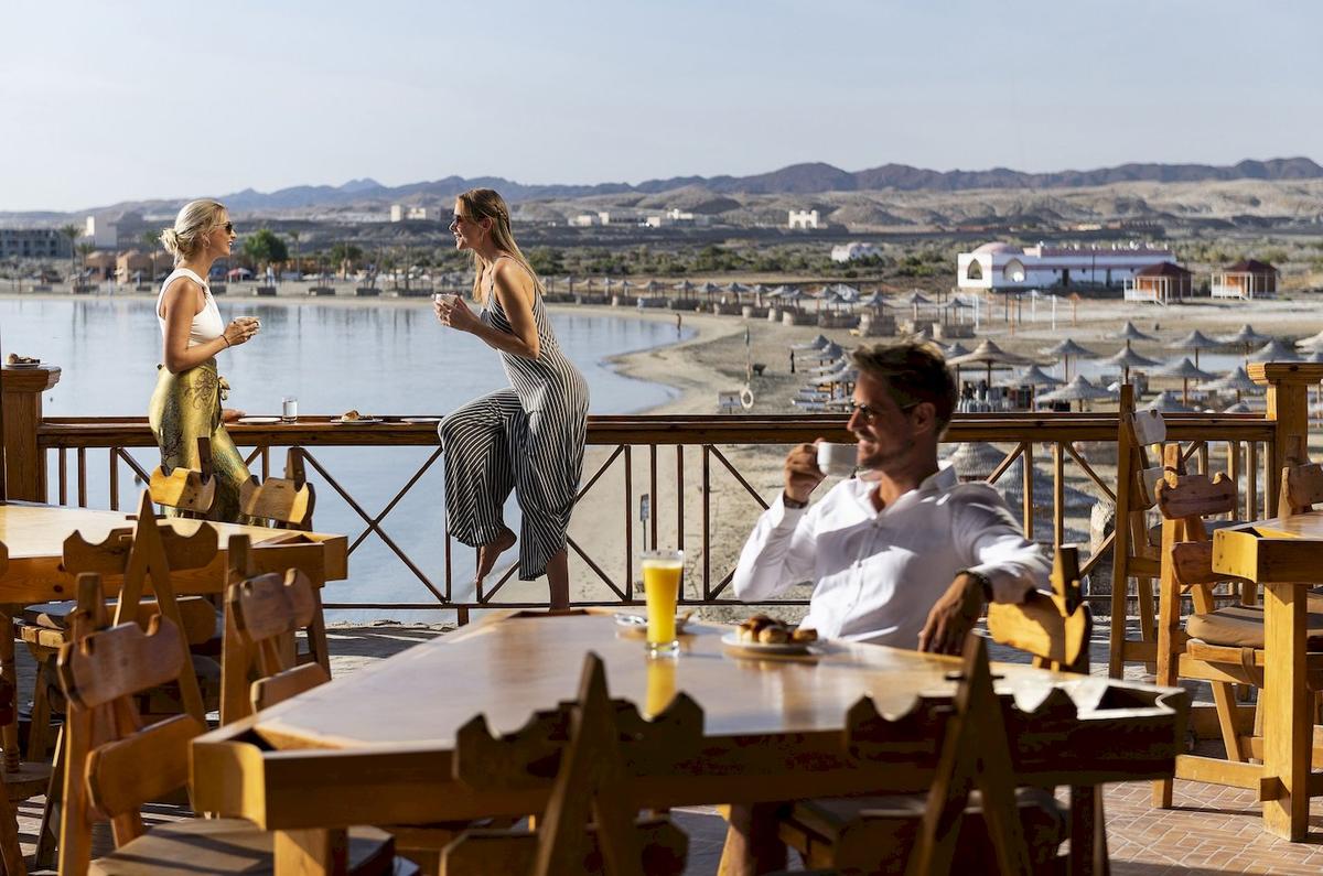 Drei Gäste sitzen auf der Terrasse des Three Corners Equinox Beach Resorts und genießen Getränke und Ausblick.