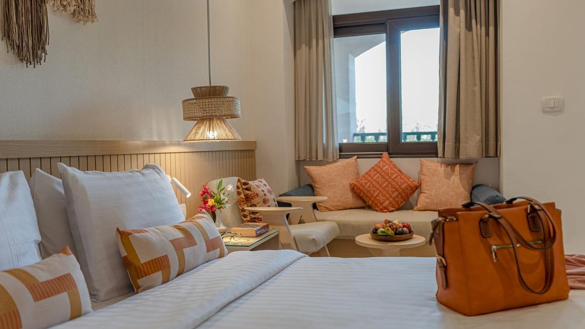 Innenansicht eines Zimmers im Three Corners Rihana Resort mit einem Bett, Kissen, einem Tisch mit Früchten und einer Tasche.