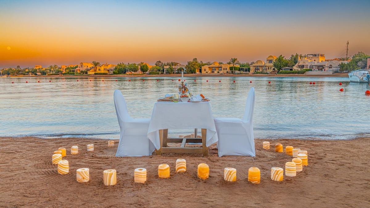 Romantisches Essen am Strand im Three Corners Rihana Resort mit einem Tisch und zwei Stühlen, umgeben von Kerzen auf dem Sand.