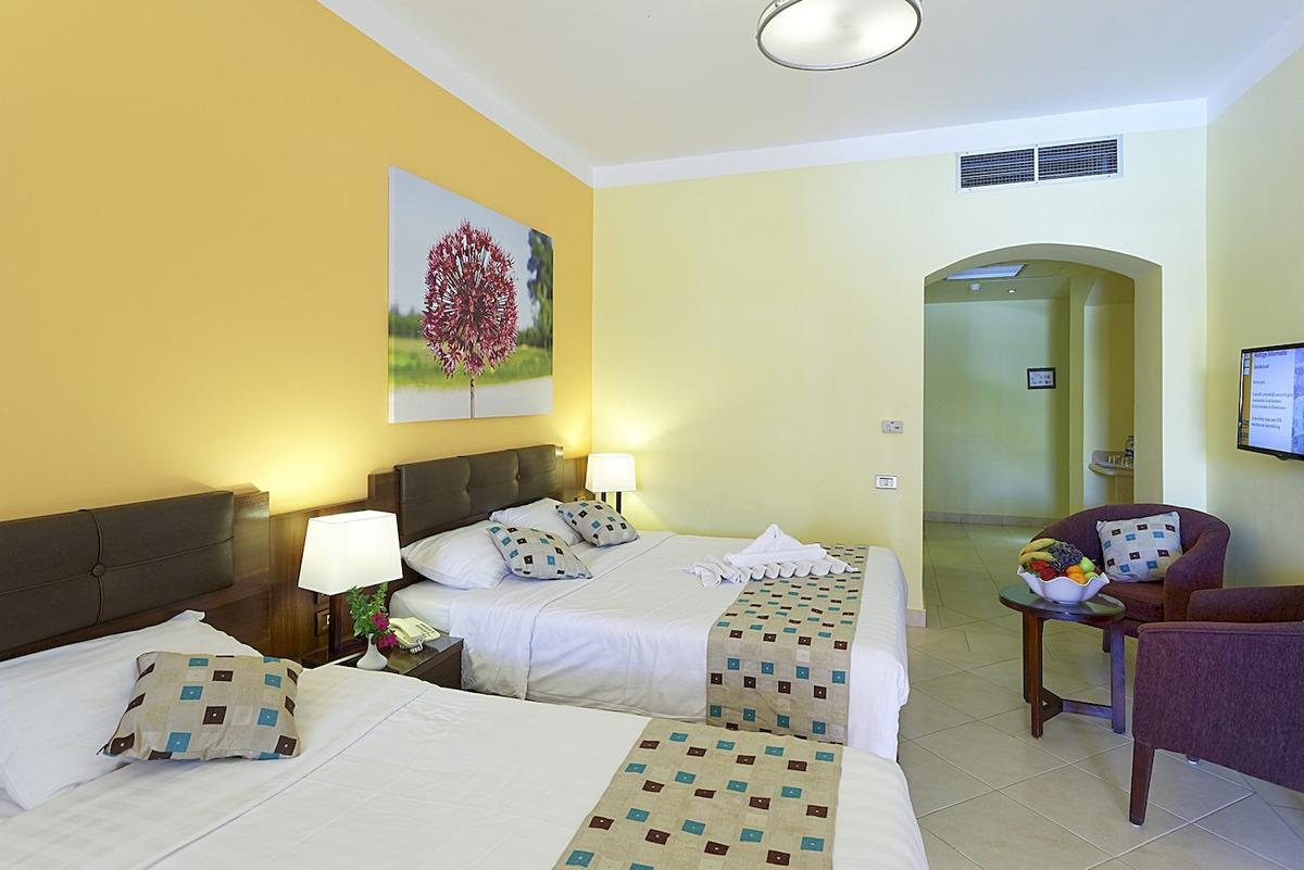 Doppelzimmer mit zwei Betten im Drei Ecken Rihana Resort, gelblich-weiße Wände und eine Blume auf dem Bild.