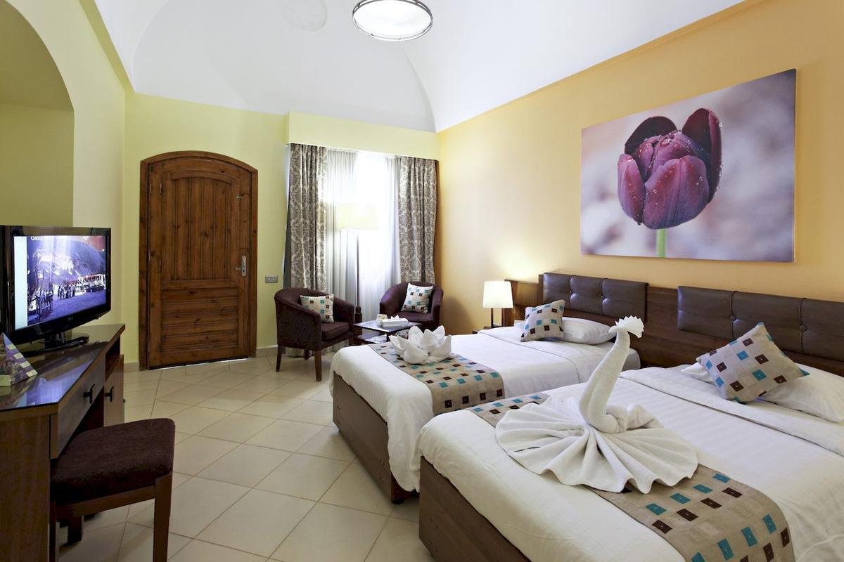 Innenansicht eines Doppelzimmers im Three Corners Rihana Resort mit zwei Betten, Fernseher, und Möbeln.