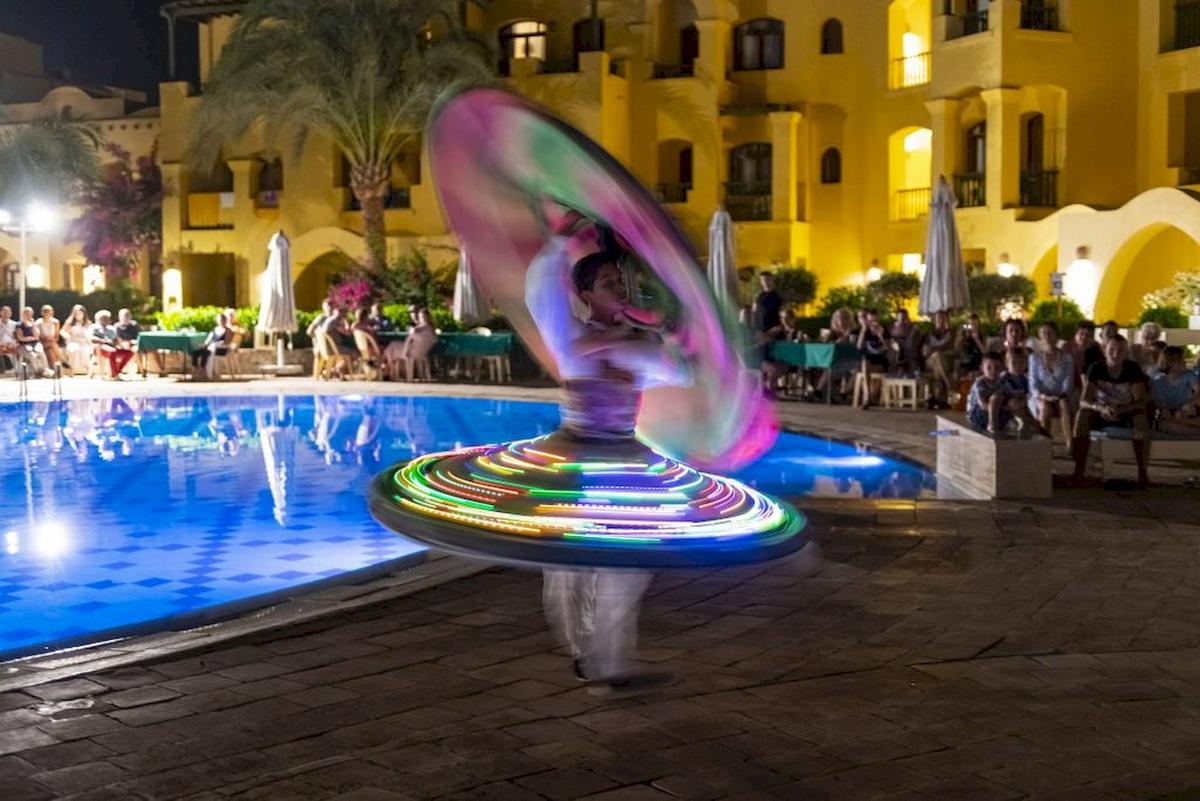 Bei Nacht tanzt eine Person mit einem leuchtenden Hula-Hoop-Reifen vor dem Pool des Three Corners Rihana Resorts.