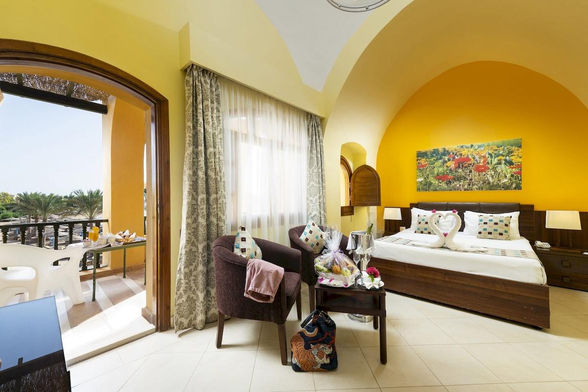 Drei-Ecken-Rihana-Resort-Hotelzimmer mit Balkon, zwei Stühlen, Tisch und Bett.