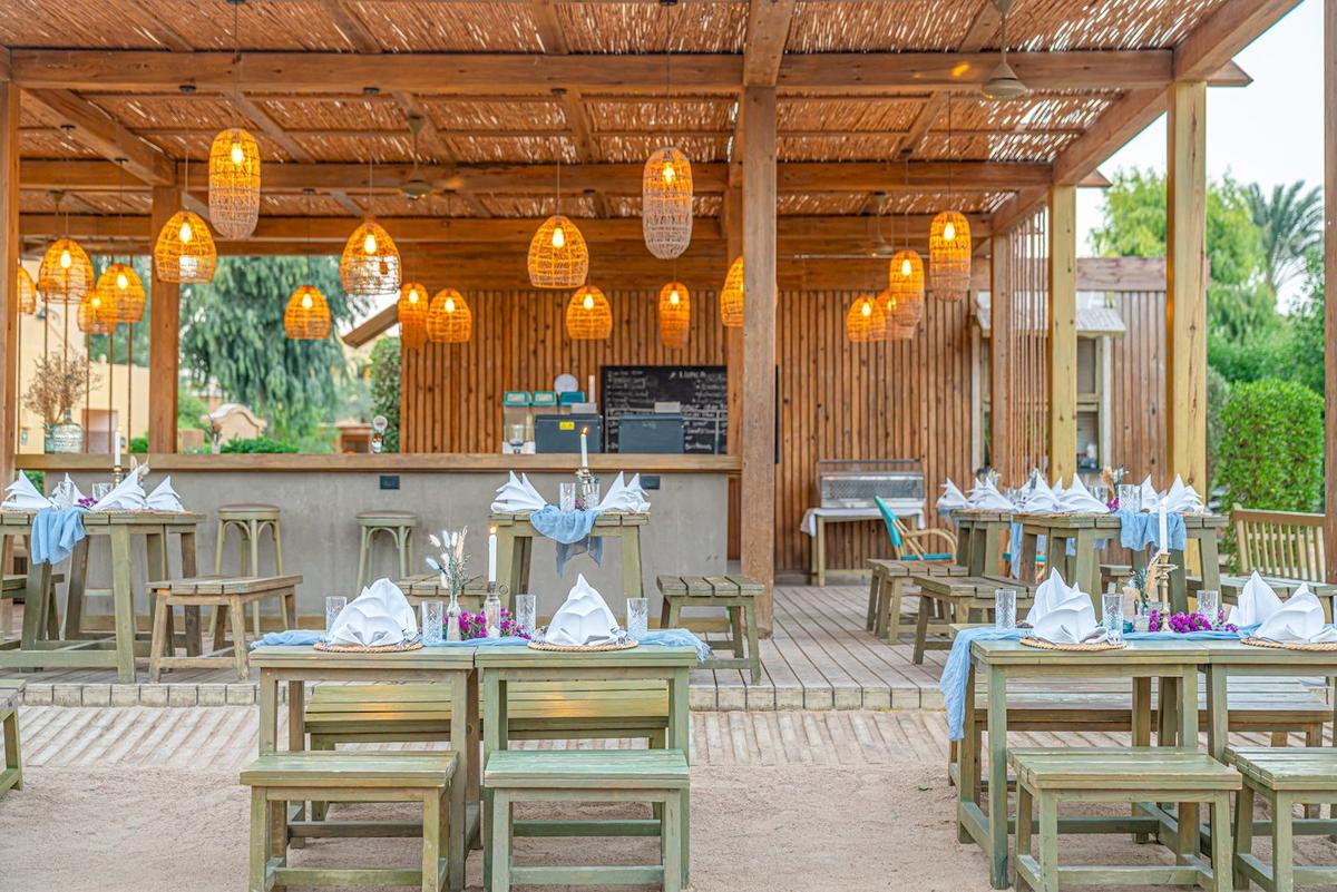 Restaurantbereich im Three Corners Rihana Resort mit Holztischen, Stühlen und Lampen.