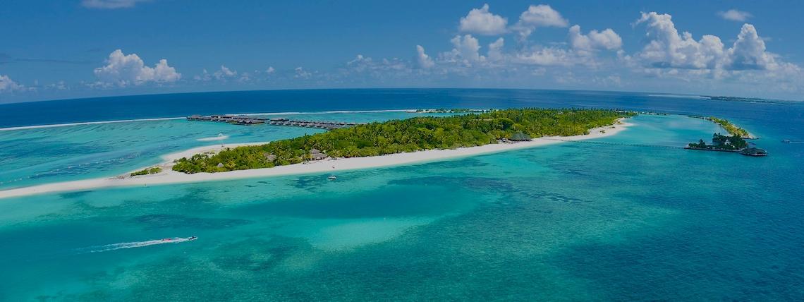 Luftaufnahme des Royal Island Resort & Spa mit weißer Sandinsel, blauem Meer und kleinen Booten.