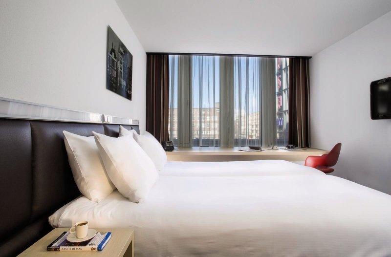 Schlafzimmer im Casa Amsterdam Hotel mit weißem Bett, Kissen und Aussicht auf die Stadt.