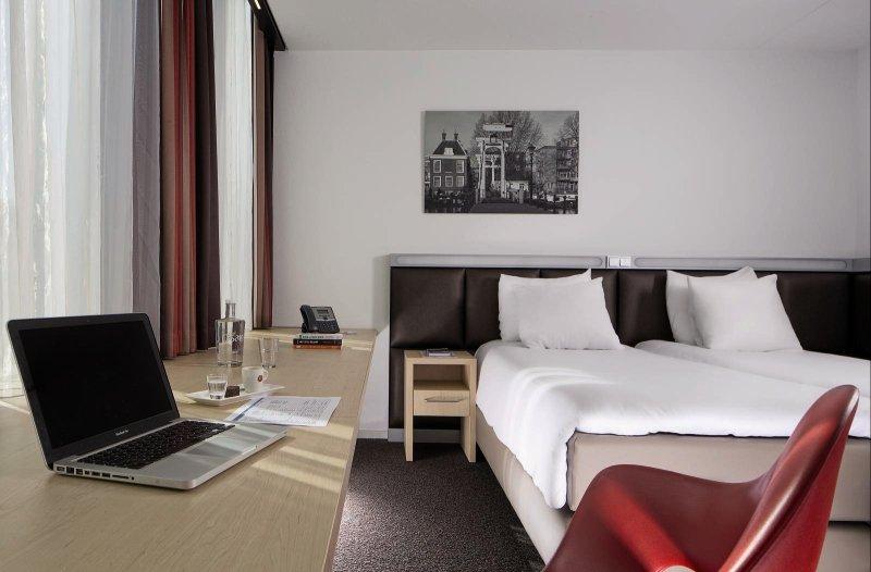 Hotelzimmer im Casa Amsterdam mit Laptop auf Schreibtisch, rotem Stuhl und zwei Betten.