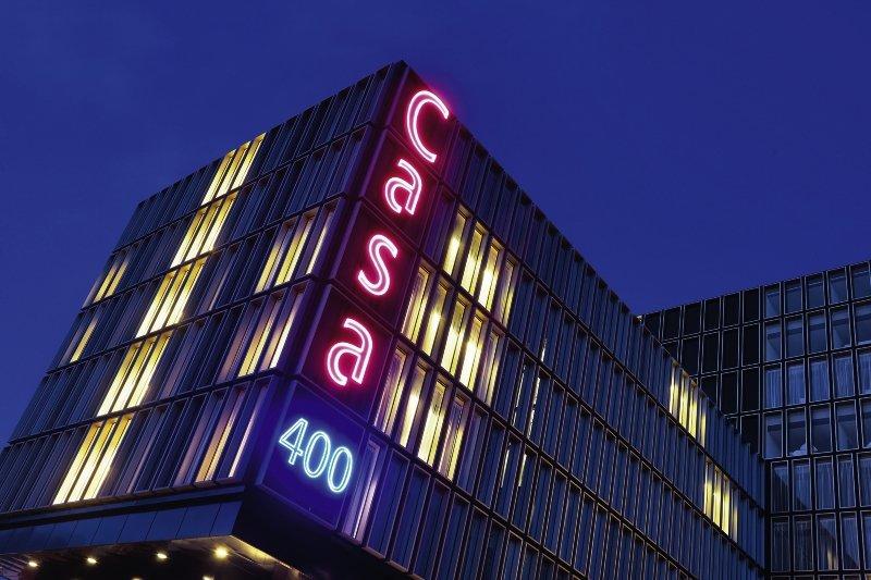 Casa Amsterdam Hochhaus bei Nacht mit blauer und pinker Beleuchtung.