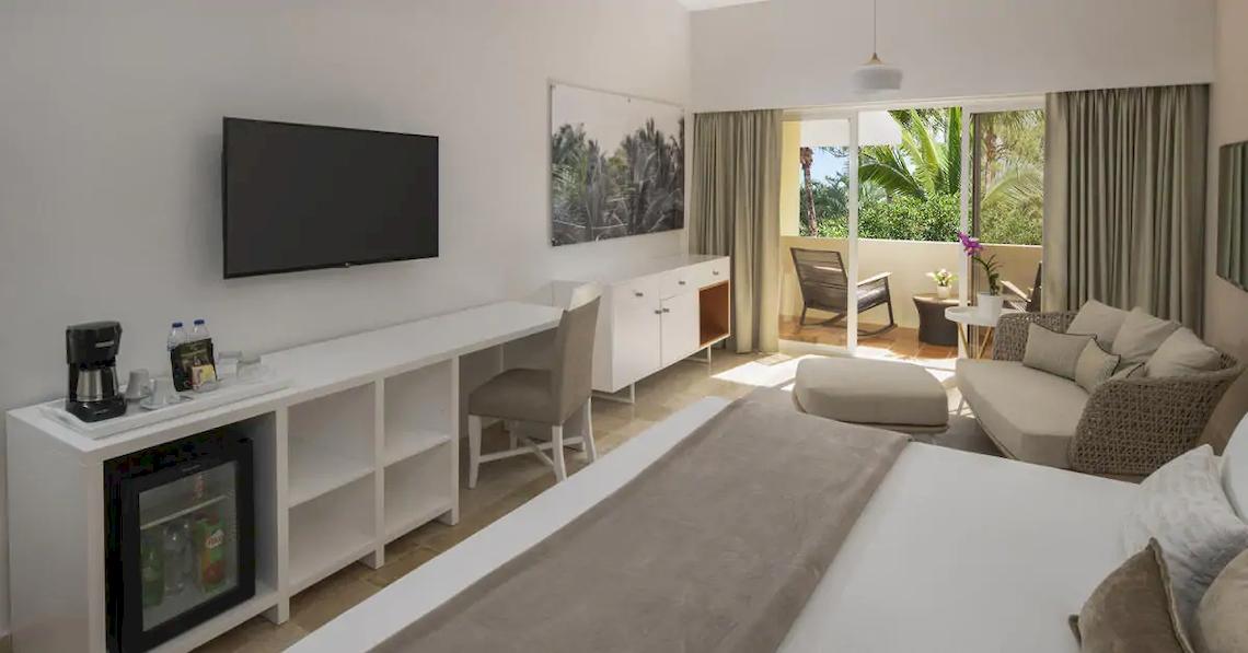 Innenansicht eines Zimmers im Melia Caribe Beach Resort mit einem Bett, Schreibtisch, Fernseher, Minibar und Balkon.