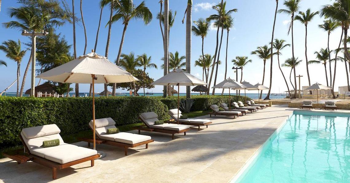 Poolbereich des Melia Caribe Beach Resorts mit weißen Liegestühlen und Palmen