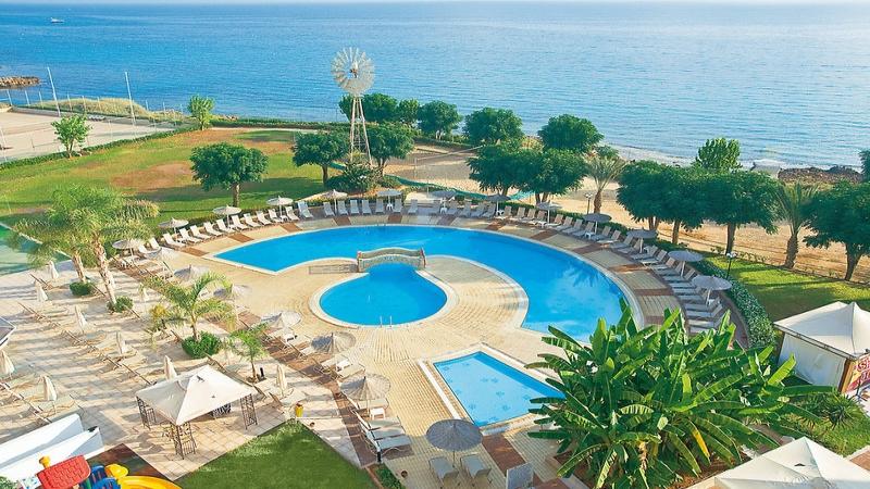 Luftaufnahme des Pernera Beach Hotels mit Swimmingpool, Sonnenliegen, Bäumen und Meer im Hintergrund.