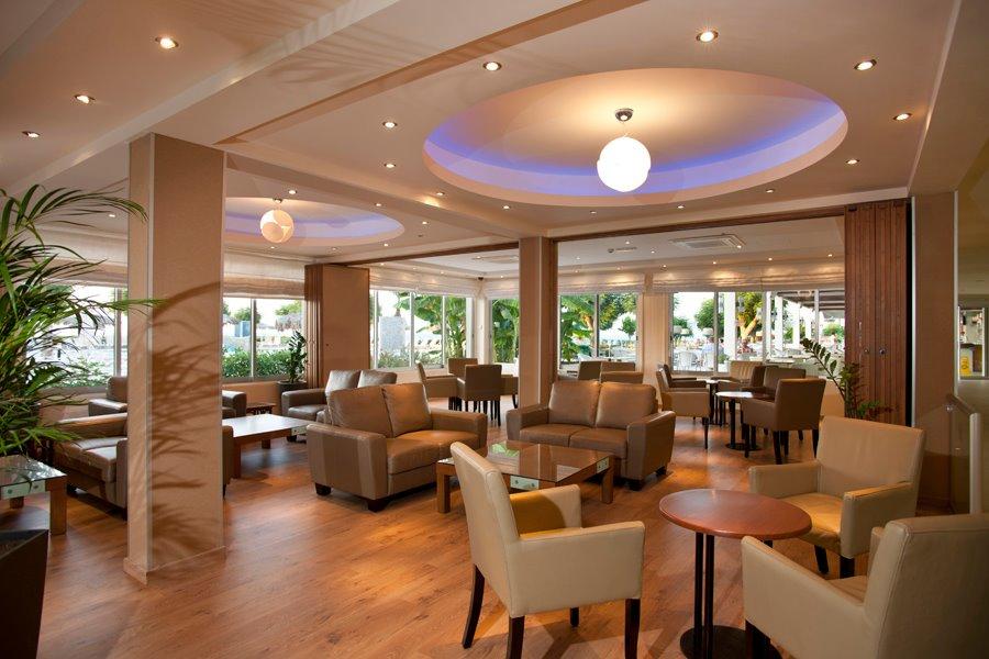 Loungebereich des Pernera Beach Hotel mit modernen Möbeln und beleuchteter Decke.