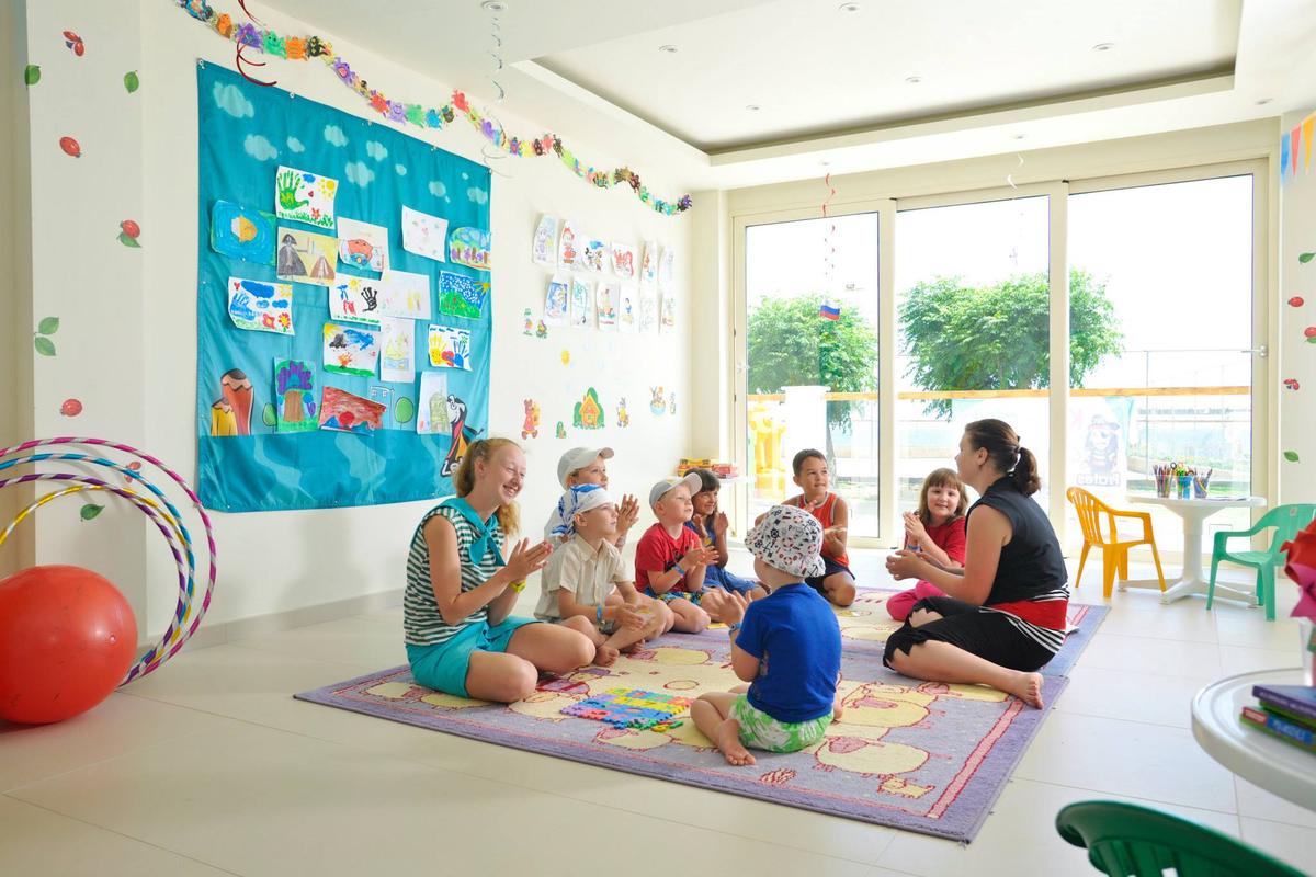 Gruppe von Kindern und zwei Erzieherinnen, die eine Runde sitzen und singen, im Pernera Beach Hotel.