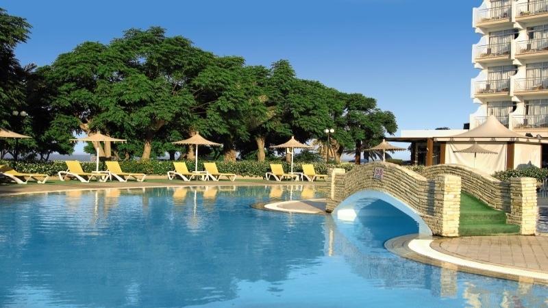 Außenpool des Pernera Beach Hotels mit gelben Liegestühlen und Sonnenschirmen.