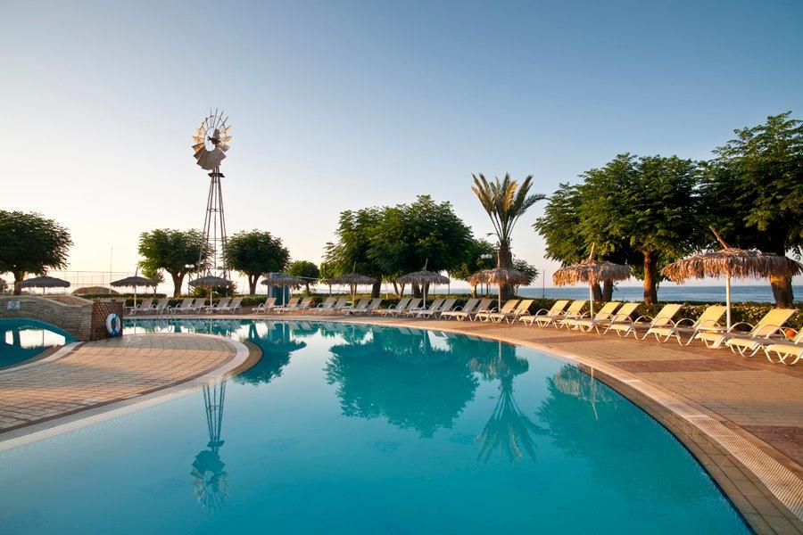Außenpool des Pernera Beach Hotel mit Sonnenliegen und Schirmen am Meer