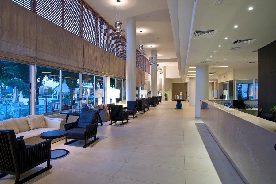 Lobby des Pernera Beach Hotels mit Sitzgelegenheiten und großen Fenstern.