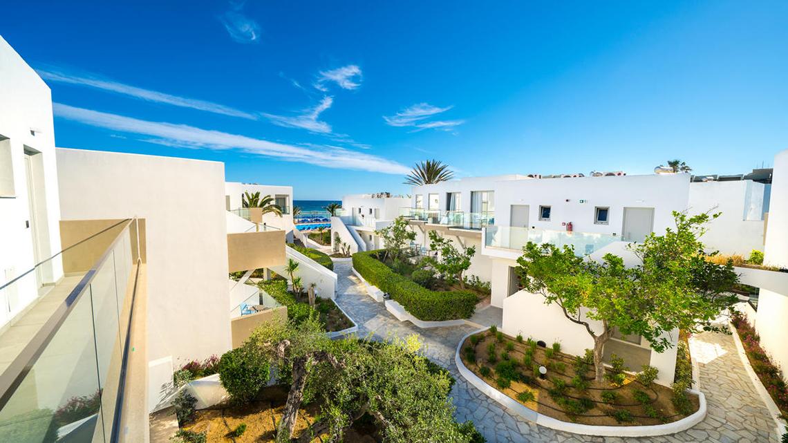 Aussenansicht des Adele Beach Hotels mit weissen Gebaeuden und Gartenanlage
