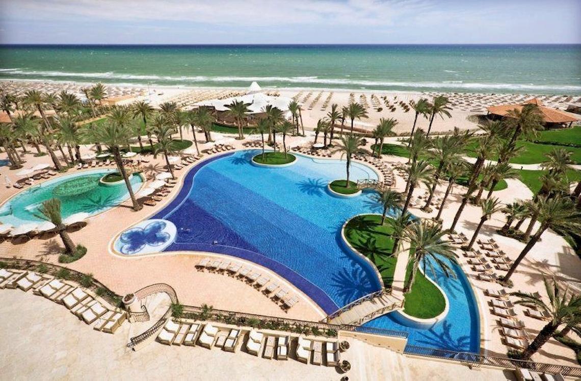 Luftaufnahme des Mövenpick Resort & Marine Spa Sousse mit zwei Swimmingpools und vielen Liegen am Strand