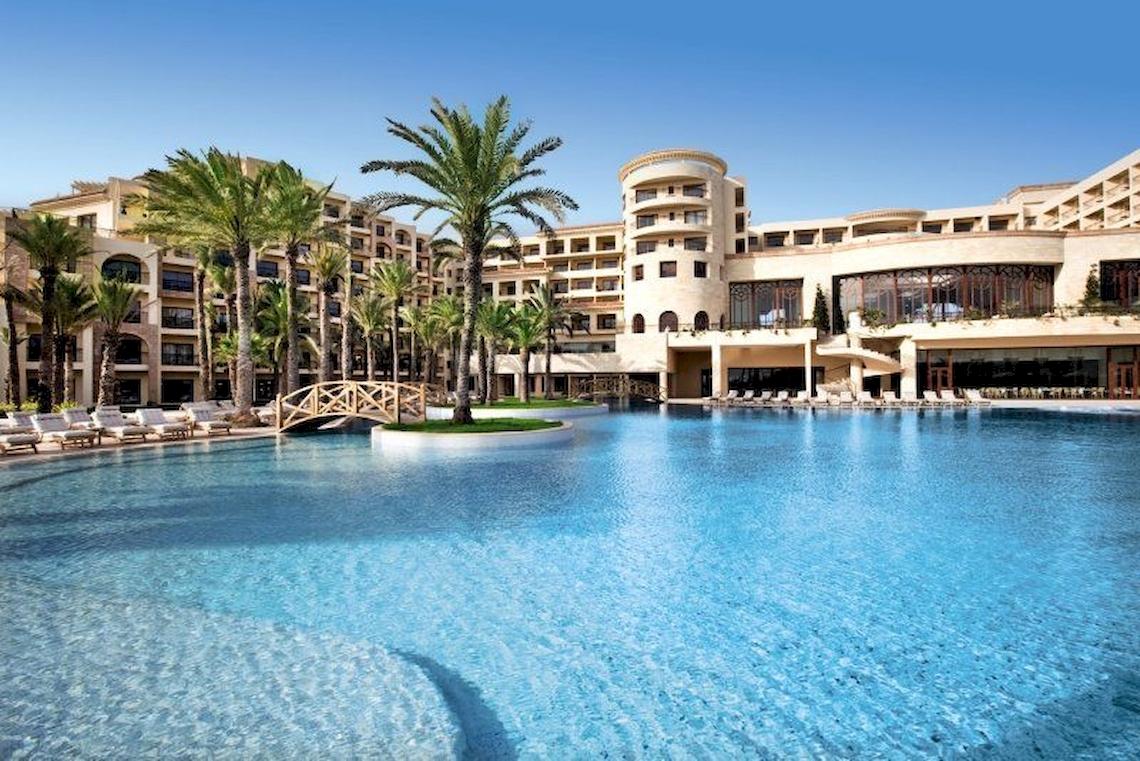 Außenansicht des Mövenpick Resort & Marine Spa Sousse mit großem Pool und Liegestühlen.