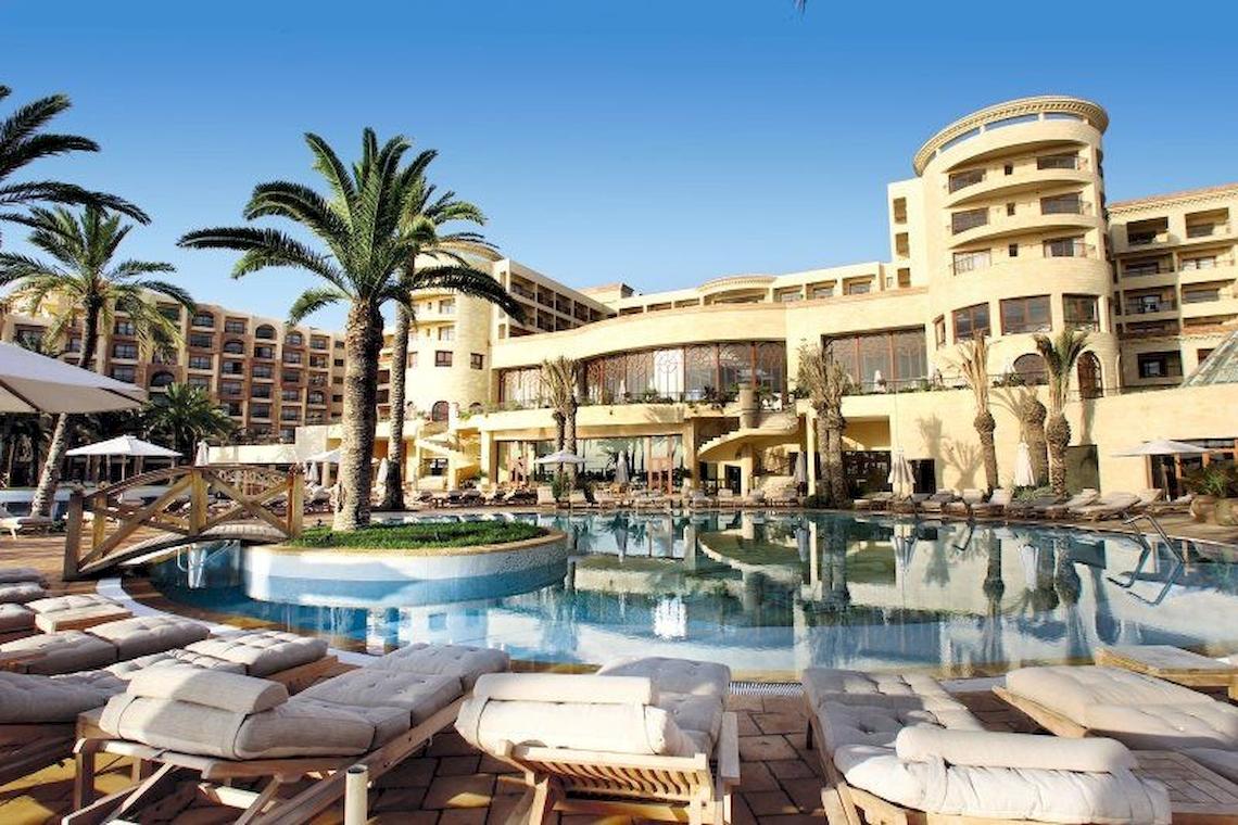 Außenansicht des Mövenpick Resort & Marine Spa Sousse mit Pool, Liegestühlen und Palmen