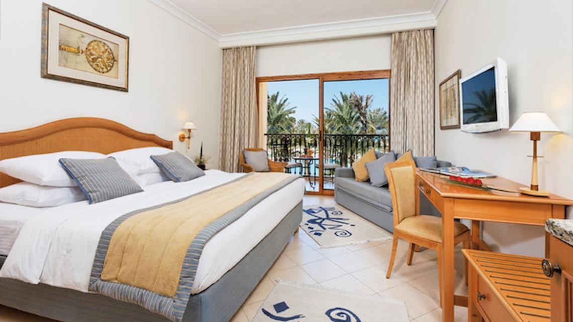 Hotelzimmer im Mövenpick Resort & Marine Spa Sousse mit großem Bett, Schreibtisch und Balkon.