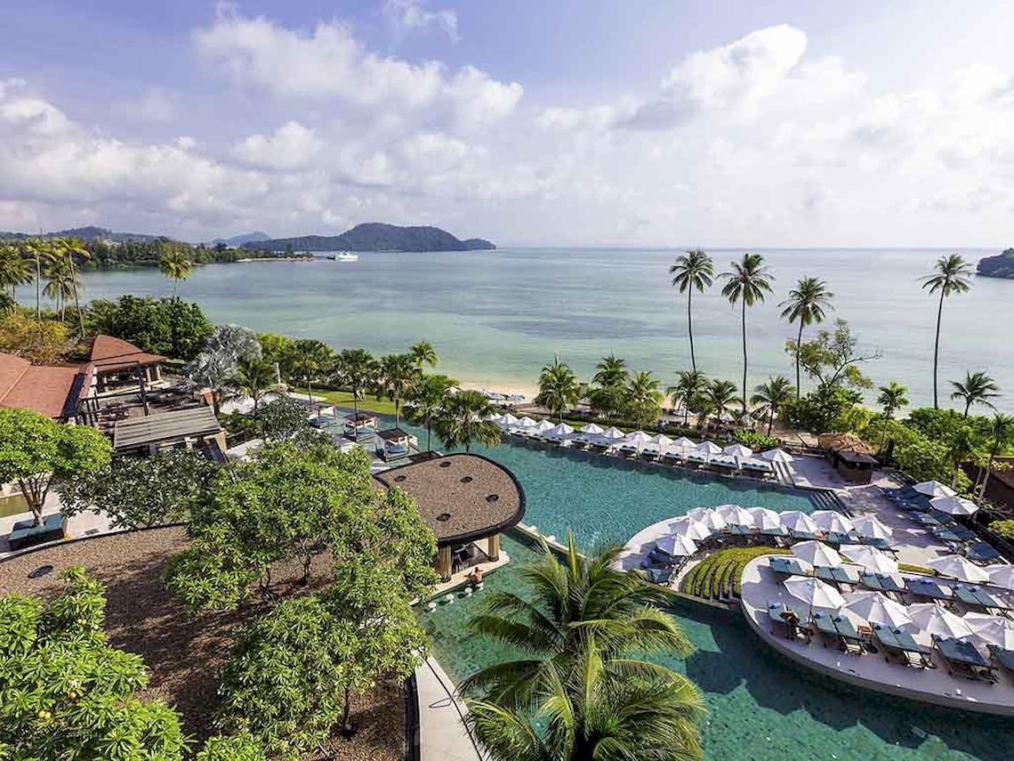 Aussicht auf das Pullman Phuket Panwa Beach Resort am Strand mit Pool und Sonnenschirmen.