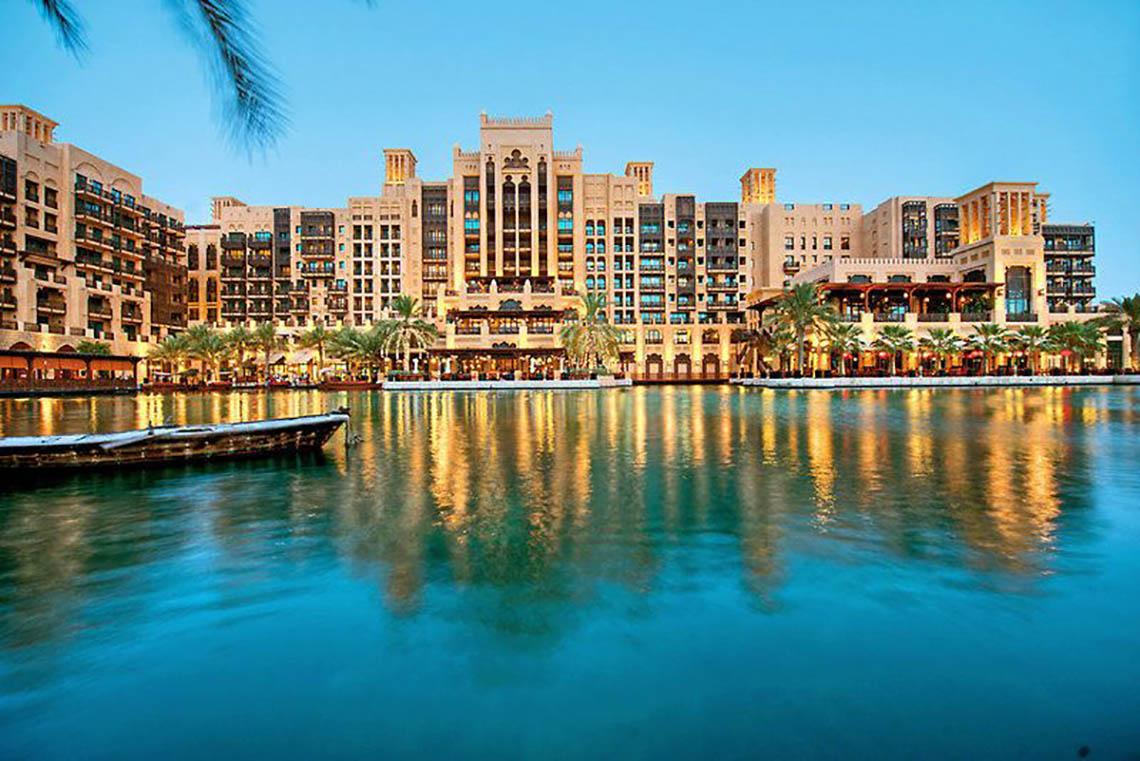 Jumeirah Dar Al Masyaf Hotel am Wasser mit Boot und Palmen im Vordergrund