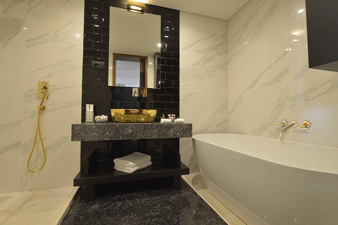 Luxuriöses Badezimmer im Domes of Elounda, Autograph Collection mit Marmorfliesen und goldenen Armaturen.
