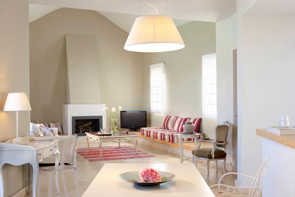 Wohnbereich im Domes of Elounda, Autograph Collection mit Kamin, Sofa, Fernseher und Tisch mit Blume.