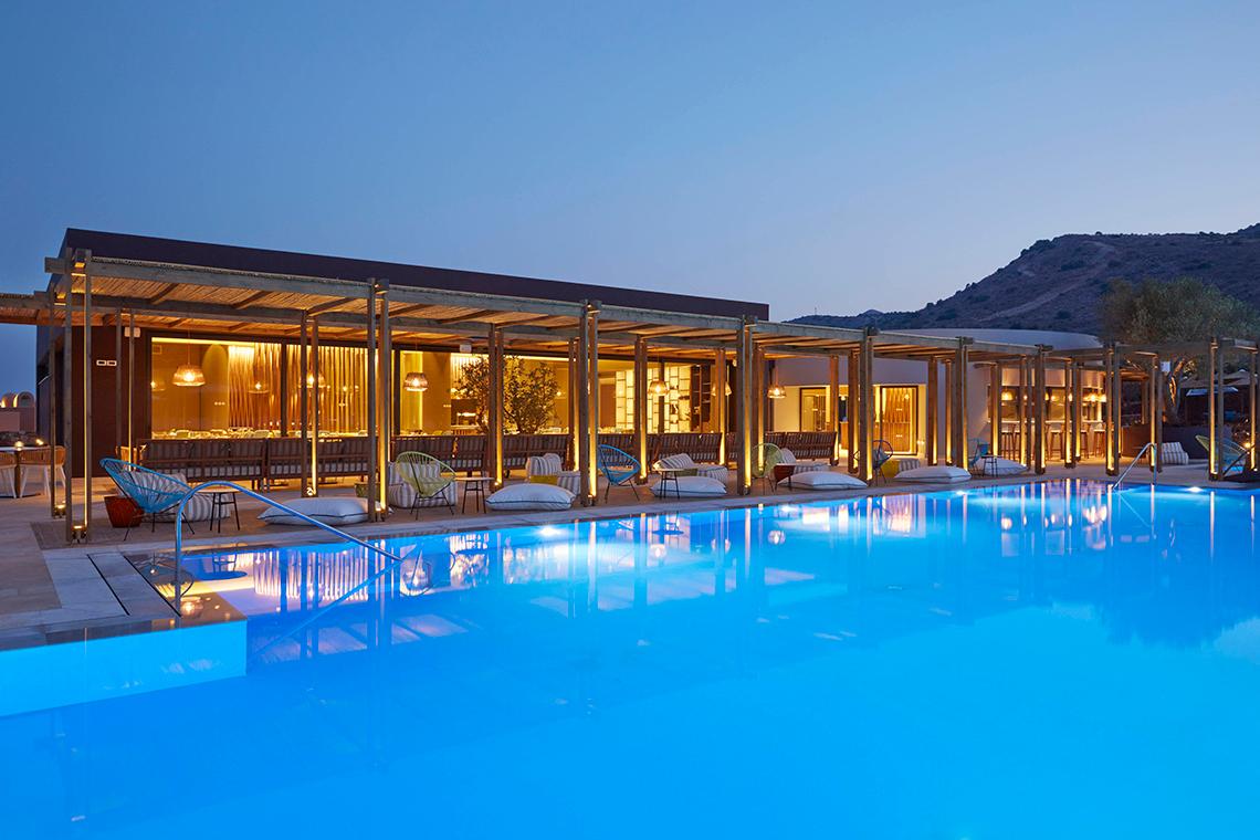 Außenbereich des Domes of Elounda Hotels mit Pool und Loungestühlen bei Nacht