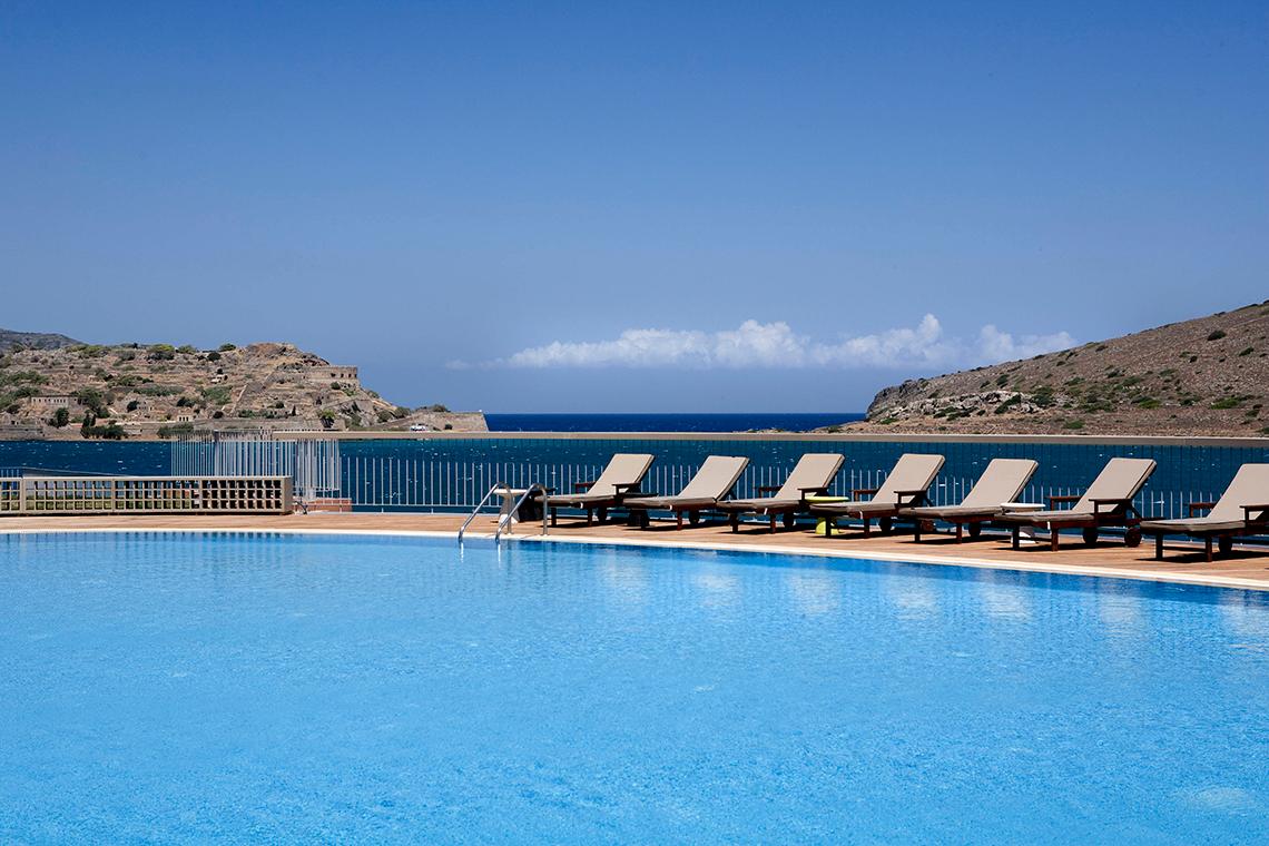 Pool am Domes of Elounda mit Blick auf das Meer und Hügel im Hintergrund