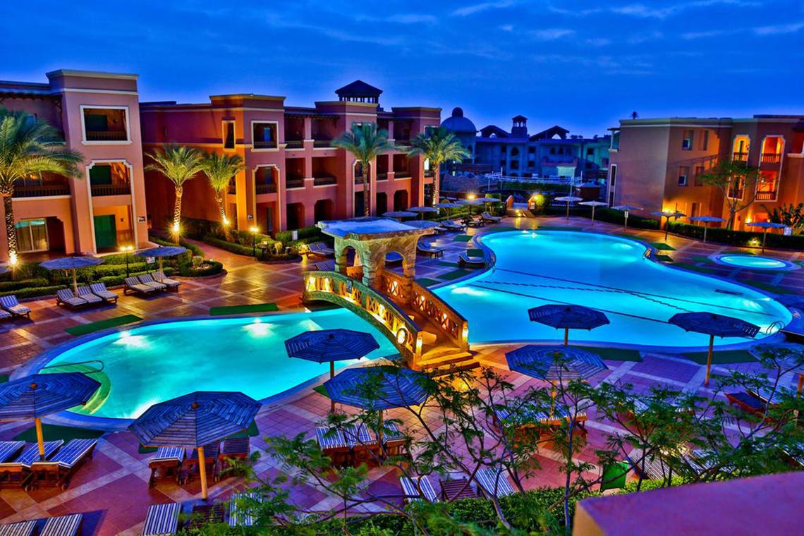 Abendliche Außenansicht des Charmillion Club Aqua Park Hotels mit Swimmingpool und Loungebereichen.