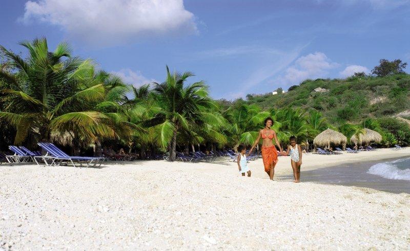 Familie am Strand des Blue Bay Curacao Golf & Beach Resorts, umgeben von Palmen und Sonnenliegen.