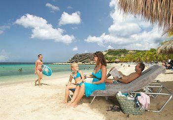 Familie am Strand des Blue Bay Curacao Golf & Beach Resorts mit Liegen und Kindern, die spielen