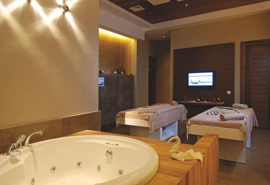 Massageraum im Commodore Elite Suites & Spa mit Badewanne, Massageliegen und Fernseher.