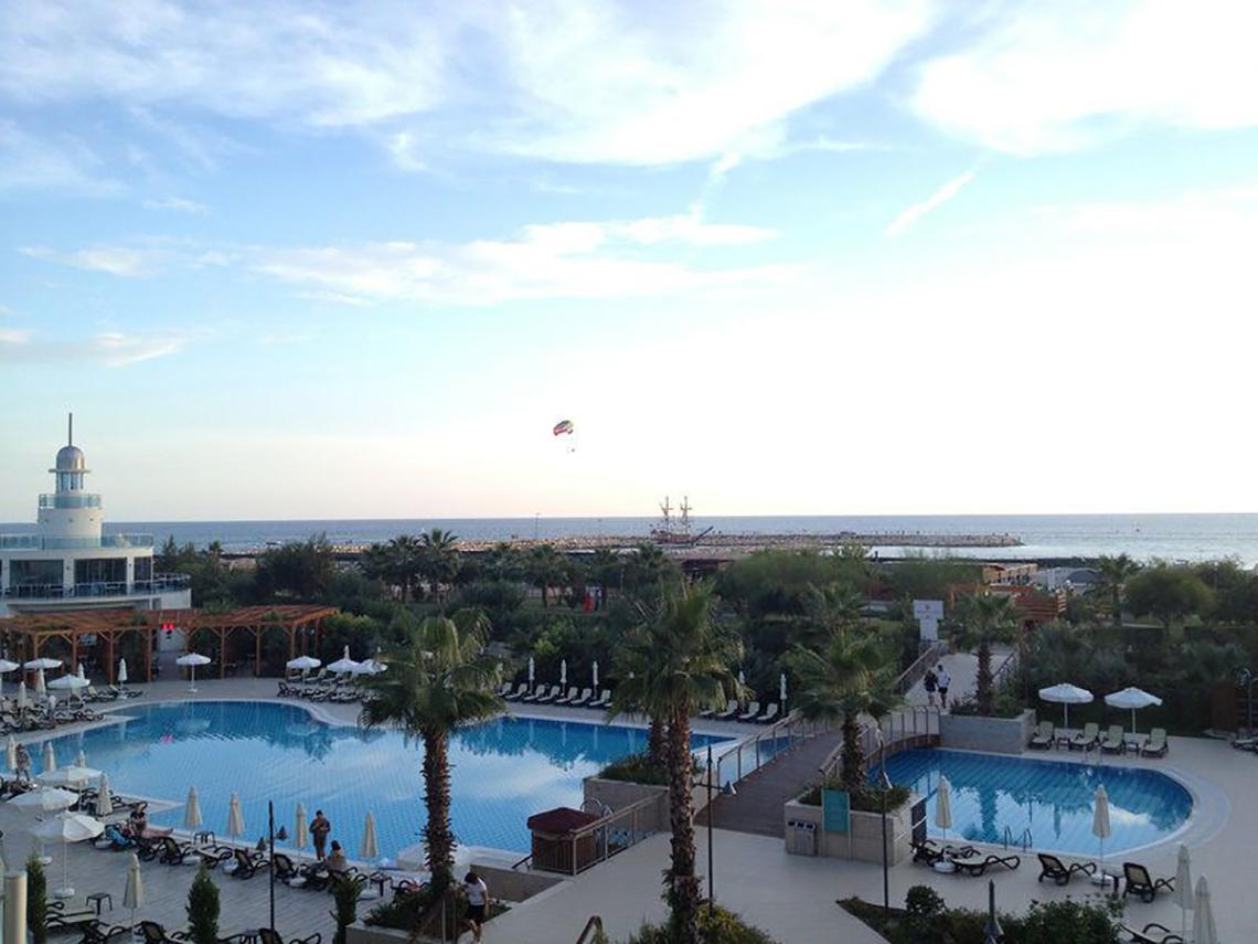 Aussicht auf das Commodore Elite Suites und Spa mit zwei Pools, Liegestühlen und Palmen am Meer.
