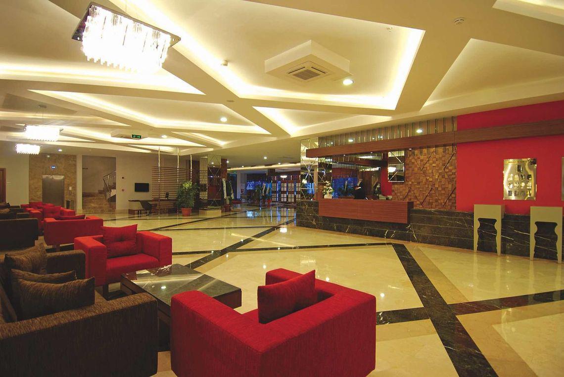Lobby des Commodore Elite Suites & Spa Hotels mit roten Sesseln, Tisch und Rezeption.