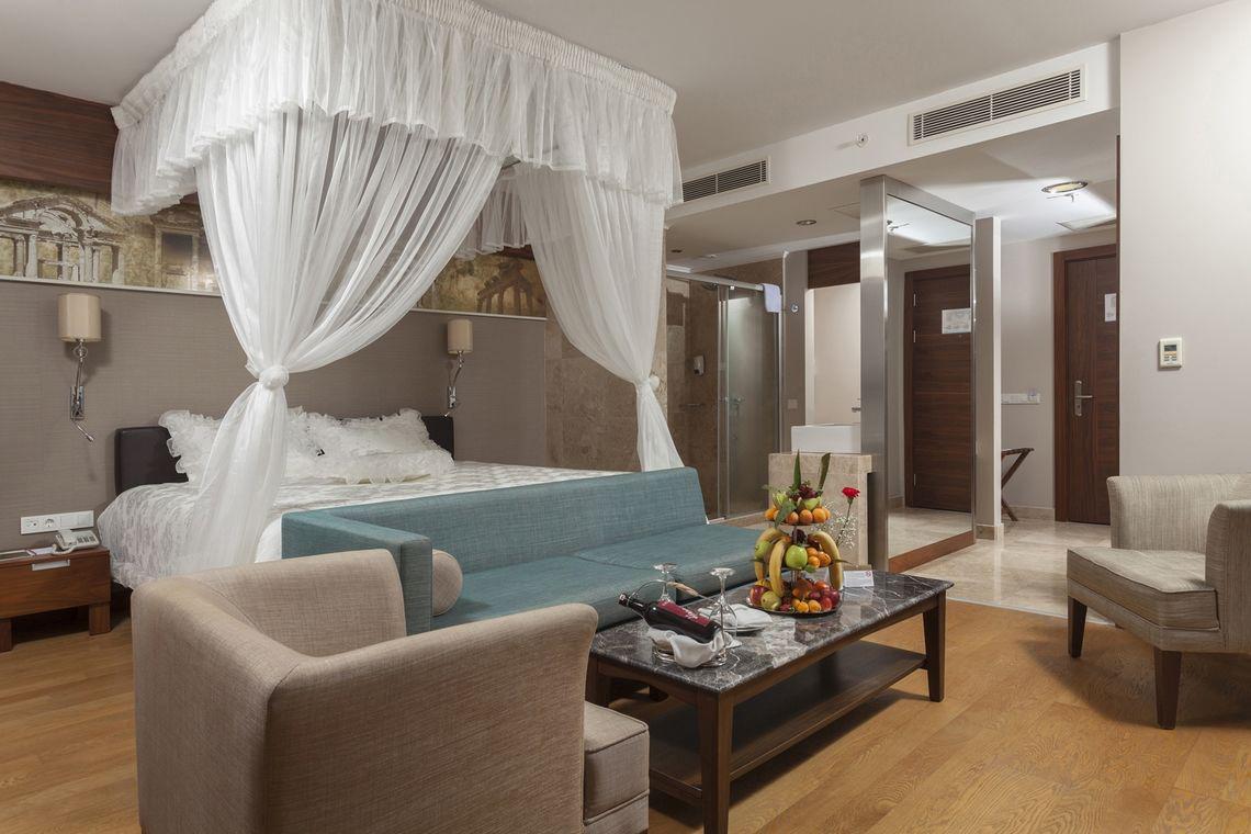 Schlafzimmer im Commodore Elite Suites & Spa mit Bett, Couch, Tisch und Früchten.