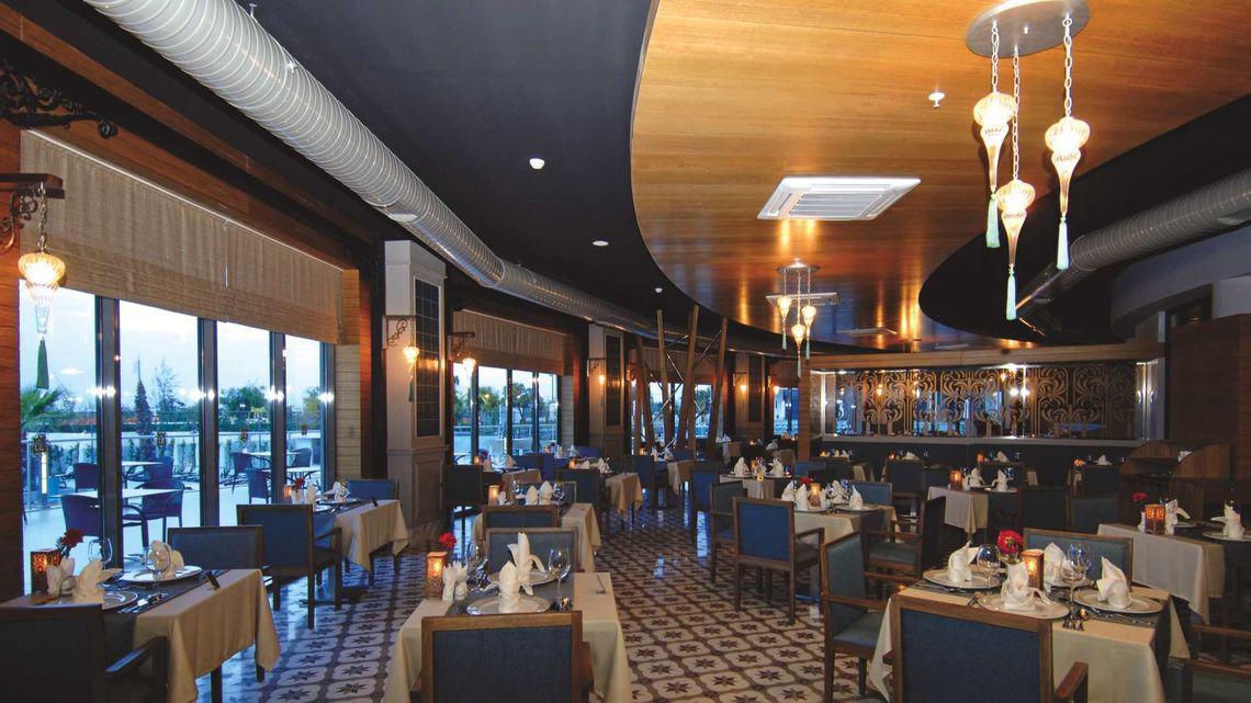 Innenansicht des Restaurants im Commodore Elite Suites & Spa mit gedeckten Tischen, dekorativen Lampen und Panoramafenstern.