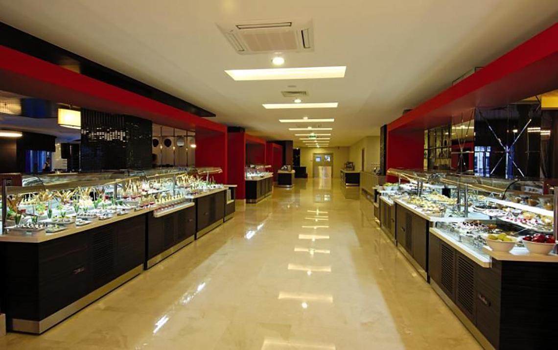 Buffet-Halle im Commodore Elite Suites & Spa Hotel mit vielen Speisen und rot-schwarzer Inneneinrichtung.