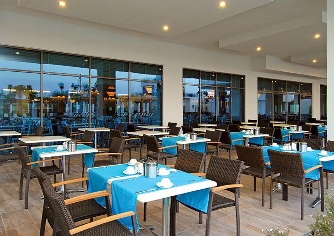 Restaurant des Commodore Elite Suites & Spa mit blauen Tischdecken und großen Fenstern.