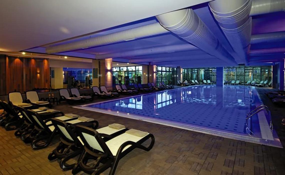 Innenpool im Commodore Elite Suites & Spa mit vielen Liegestühlen und blauer Beleuchtung.