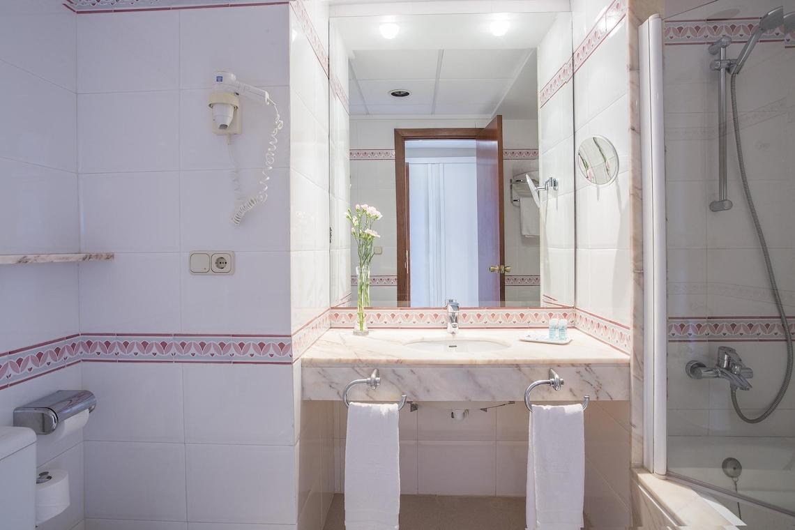 Badezimmer im Hipotels Said Hotel mit weißem Waschbecken, Spiegel und Handtüchern.