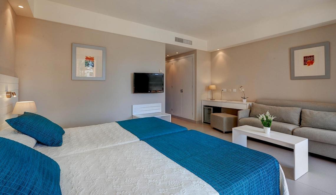 Innenansicht eines Doppelzimmers im Hipotels Said Hotel mit zwei Betten, einem Fernseher und einer Couch.