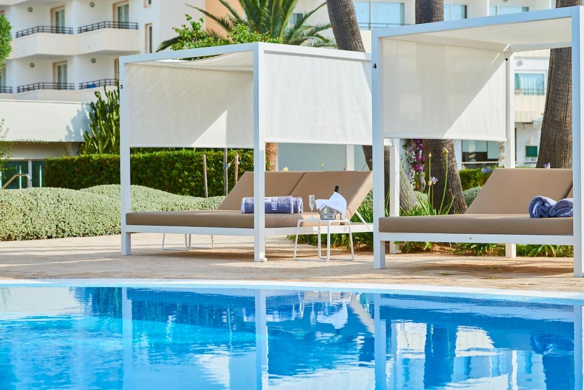 Pool-Lounge-Bereich im Hipotels Said mit zwei weißen Sonnenliegen und Überdachungen.