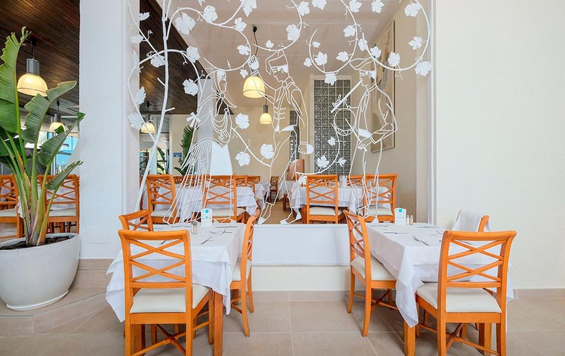 Restaurantbereich im Azuline Hotel Mar Amantis mit weißen Tischen, orangen Stühlen und Blattmustern an der Wand.