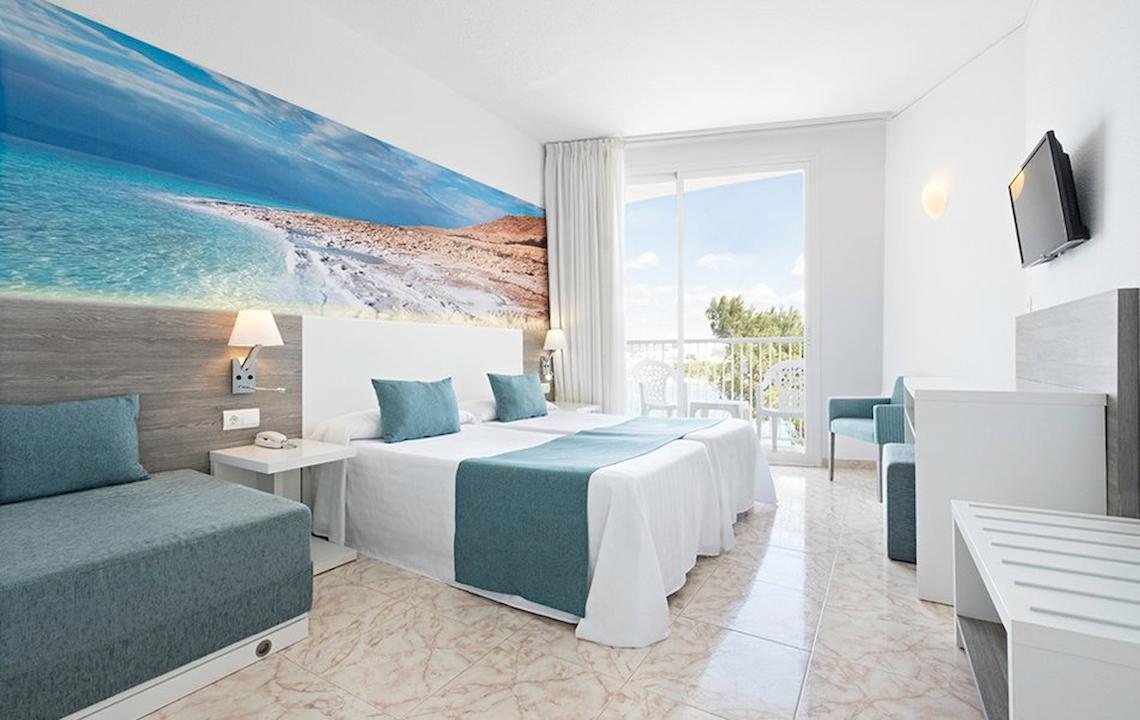 Innenansicht eines Hotelzimmers mit zwei Betten, Balkon und moderner Einrichtung.
