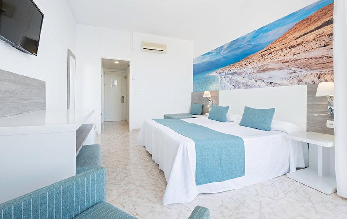 Hotelzimmer im Azuline Hotel Mar Amantis mit weißem Bett, blauen Kissen und Wandbild.