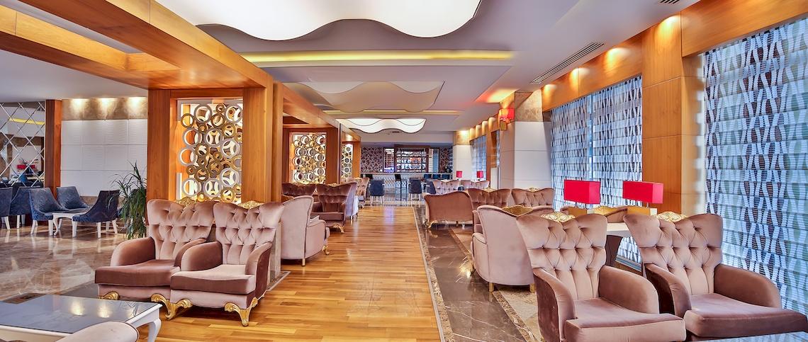 Innenansicht des Saturn Palace Resorts mit gepolsterten Stühlen, Holzboden und großen Fenstern.